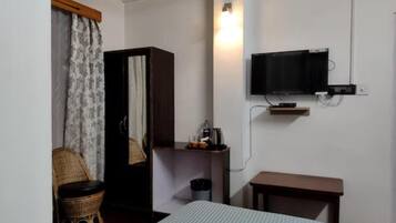 A room with a bed, a television mounted on the wall, a small table, a chair, and a wardrobe.