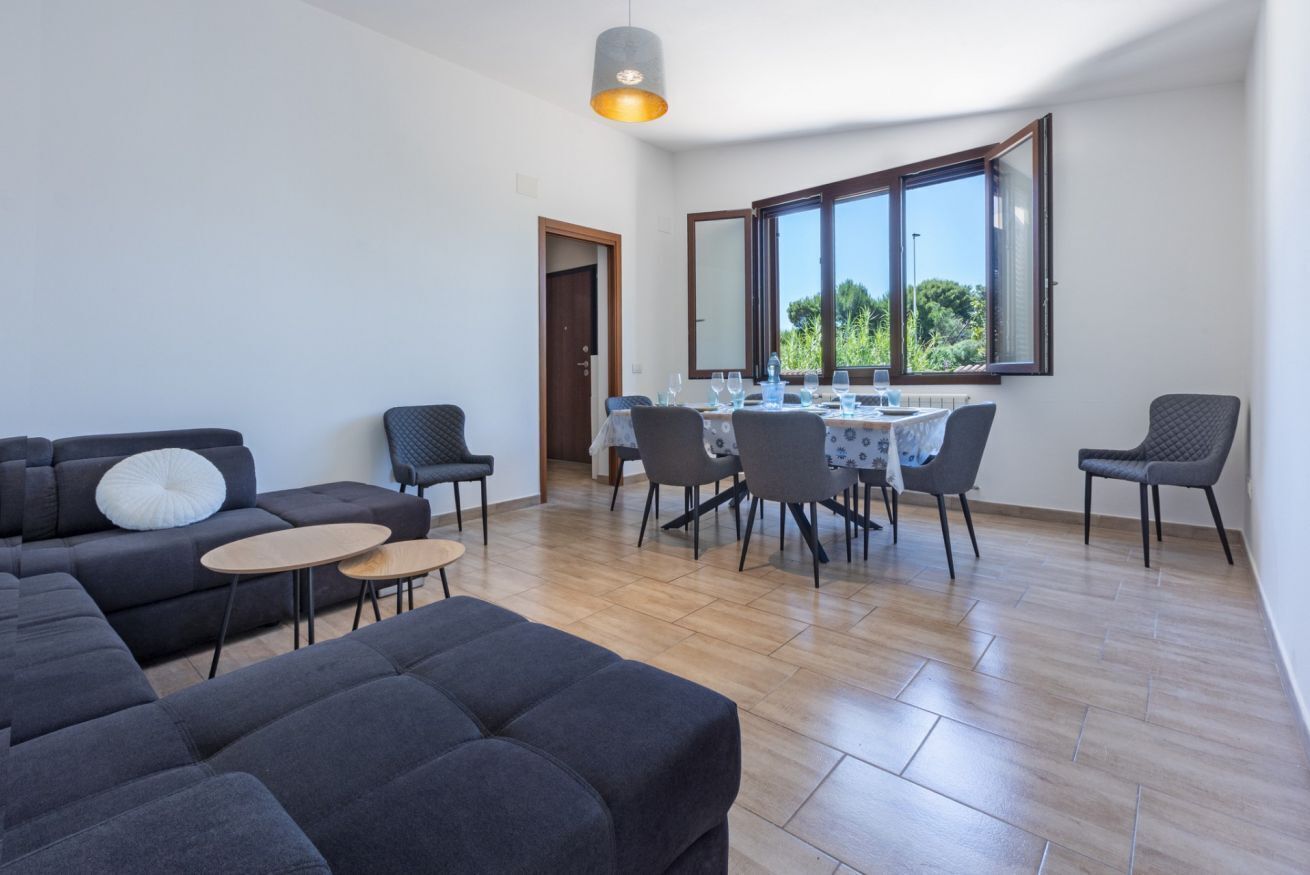 A modern living room with a sectional sofa, a dining table with chairs, and a large window with a view of greenery.