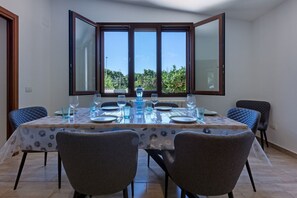 A dining area with a table set for six, large windows, and two chairs. - GuestHost - I Mandorli: A Villa Between the Sea and Downtown (Quartu Sant'Elena)