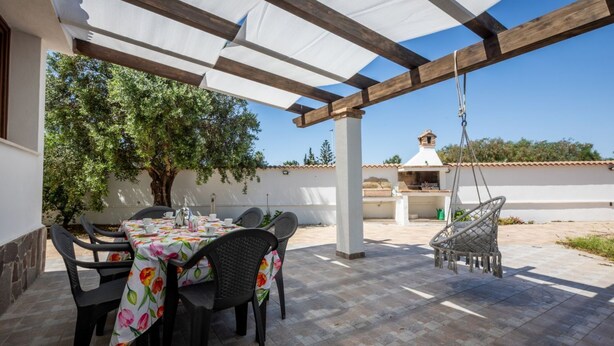 Eine Terrasse im Freien mit Esstisch, einer Hängesitzgelegenheit und einer Pergola.