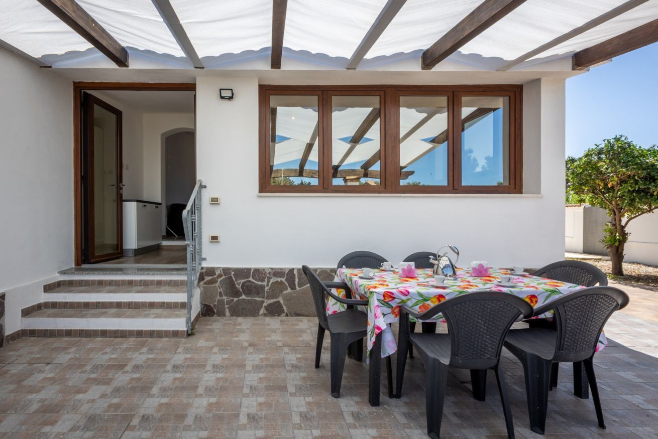 An outdoor patio with a table set for four, a stone wall, and a wooden staircase leading to an interior.