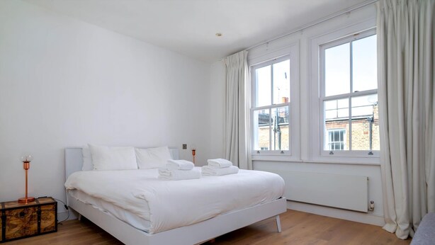 Ein Schlafzimmer mit einem weißen Bett, Holzboden und einem Fenster mit Vorhängen.