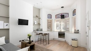 Ein kompakter Wohnraum mit Küchenzeile, Essbereich und einer Sitzecke mit Sofa und Barhocker.