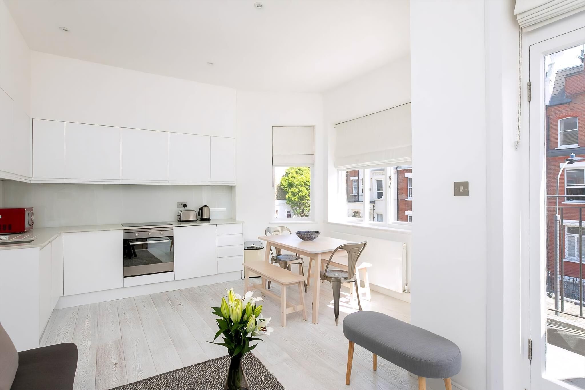 A modern kitchen with white cabinets, a built-in oven, and a dining area with a table and chairs.