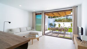 A modern living room with a sofa, coffee table, TV, and a balcony with outdoor furniture. - Villas de Punta Lara 18 by Casasol (Nerja)