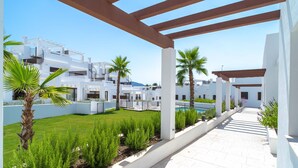 A covered outdoor area with white buildings, palm trees, and a well-maintained lawn. - Villas de Punta Lara 18 by Casasol (Nerja)