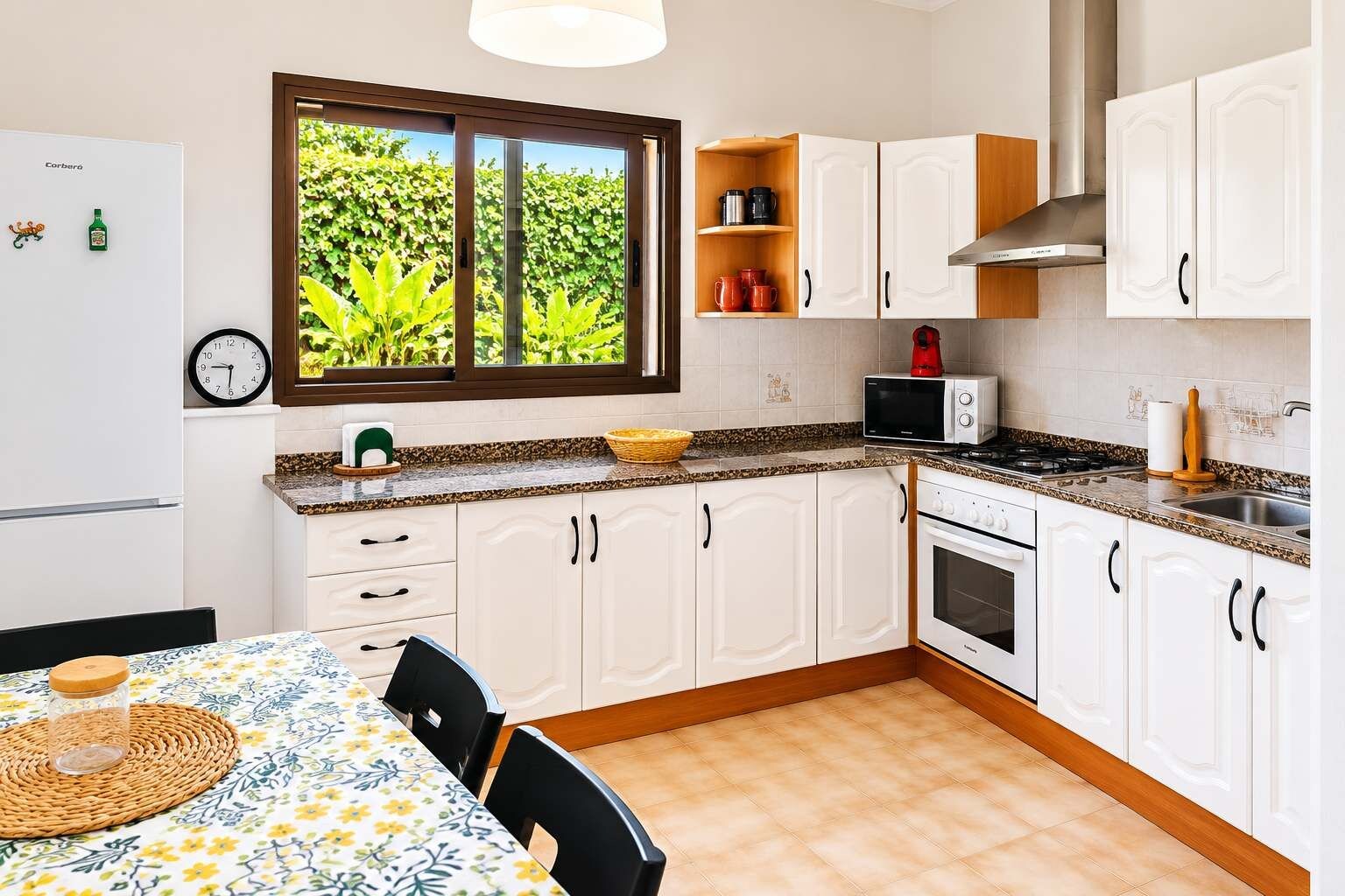 Una cocina con armarios blancos, microondas, estufa y ventana con vistas a la vegetación.