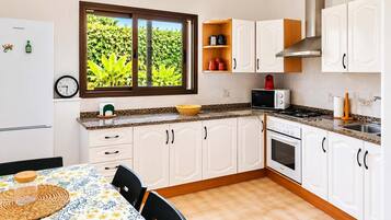 Una cocina con armarios blancos, microondas, estufa y ventana con vistas a la vegetación.