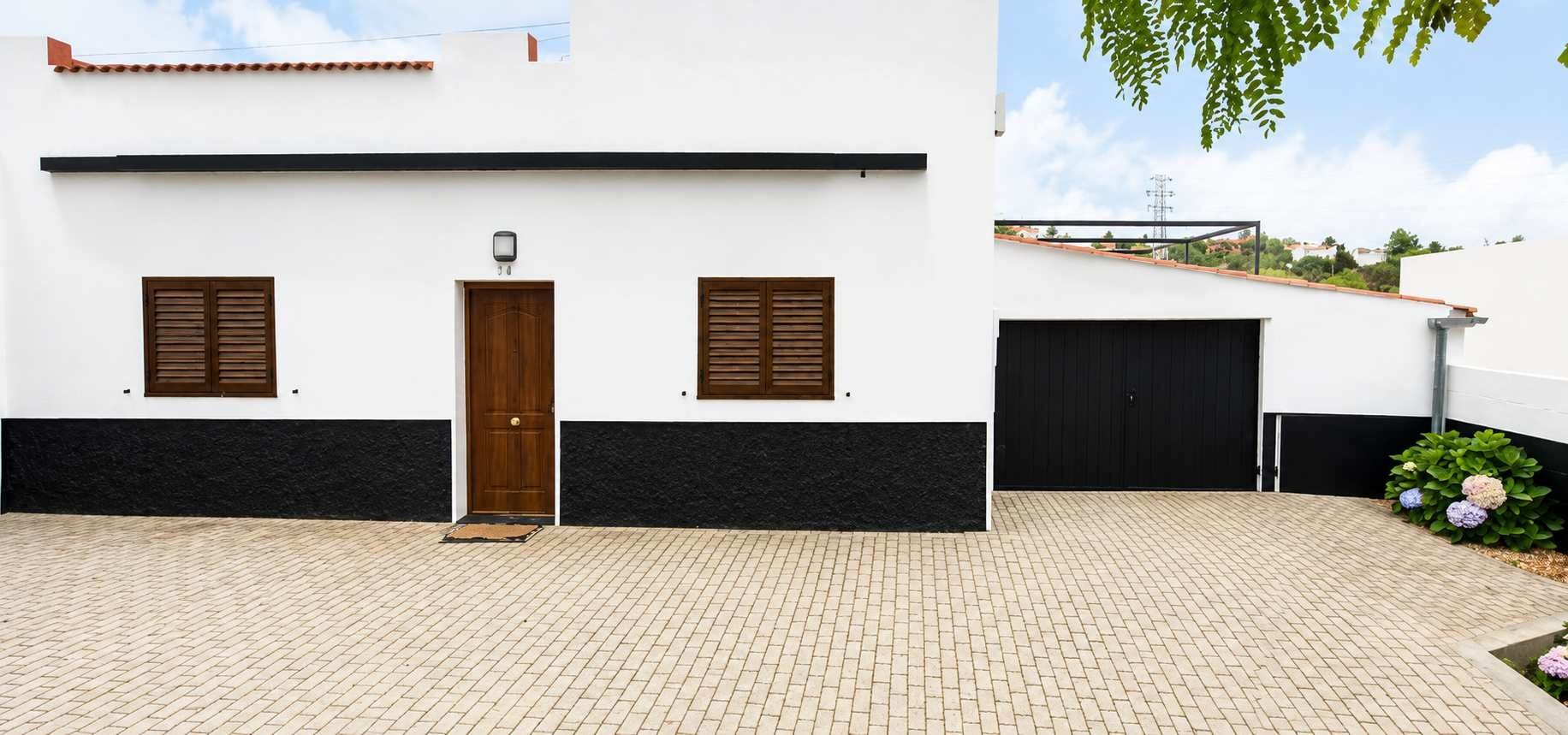 Un edificio con fachada blanca, dos puertas de madera y un portón de garaje negro.
