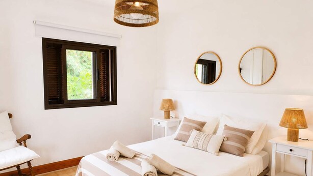 A bedroom with a bed, two bedside tables, a chair, a window with blinds, and two wall-mounted mirrors. - Casa del Parque Tacoronte Centro (Tacoronte)