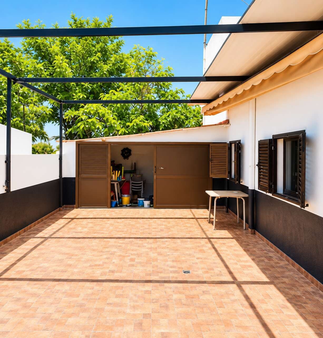 A covered outdoor area with a tiled floor, a storage unit with a door, and a table.