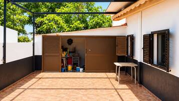 A covered outdoor area with a tiled floor, a storage unit with a door, and a table.