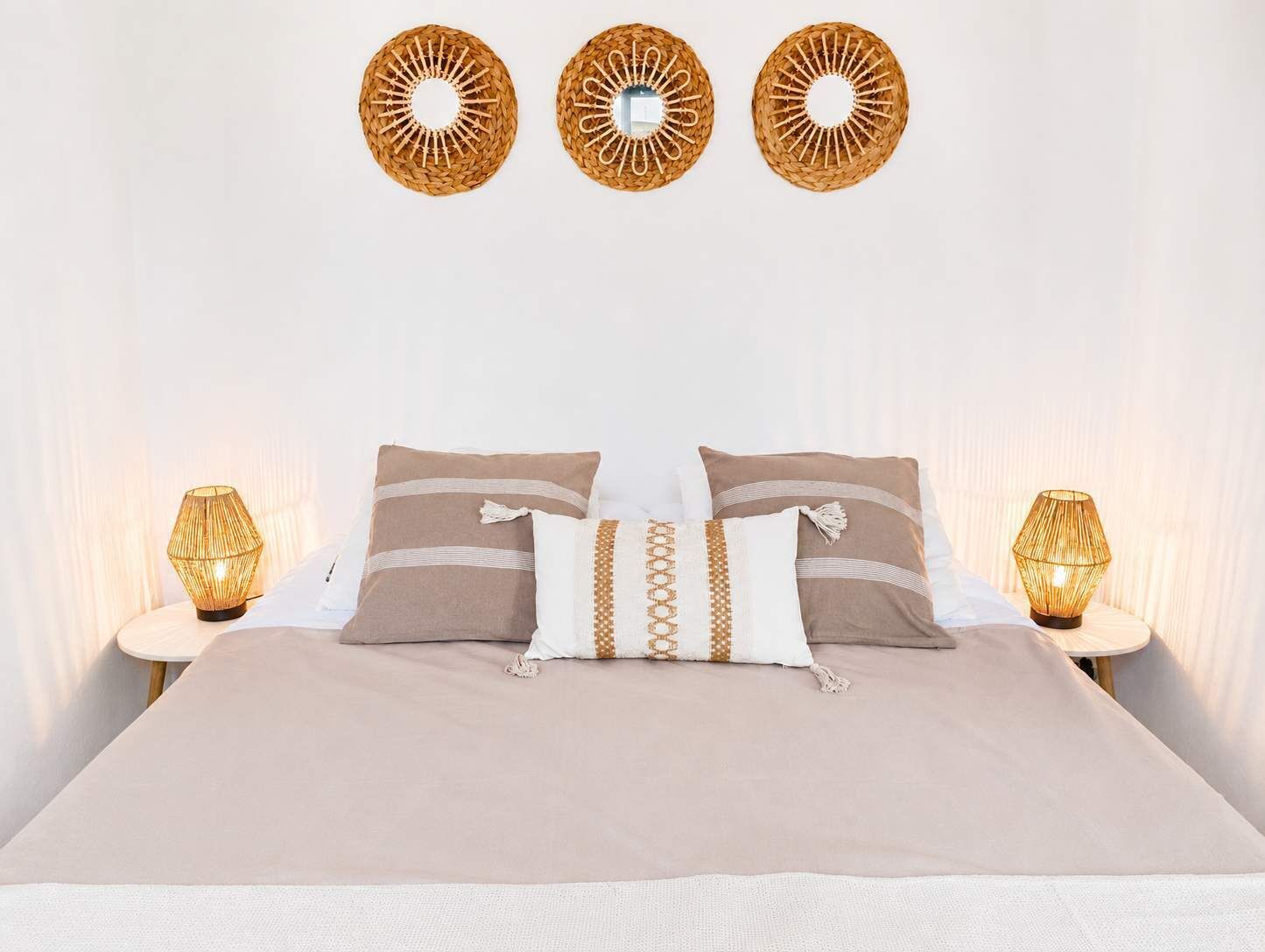 Un lit recouvert d’une couvre-lit beige, deux oreillers ornés de motifs décoratifs et trois lampes fixées au mur.