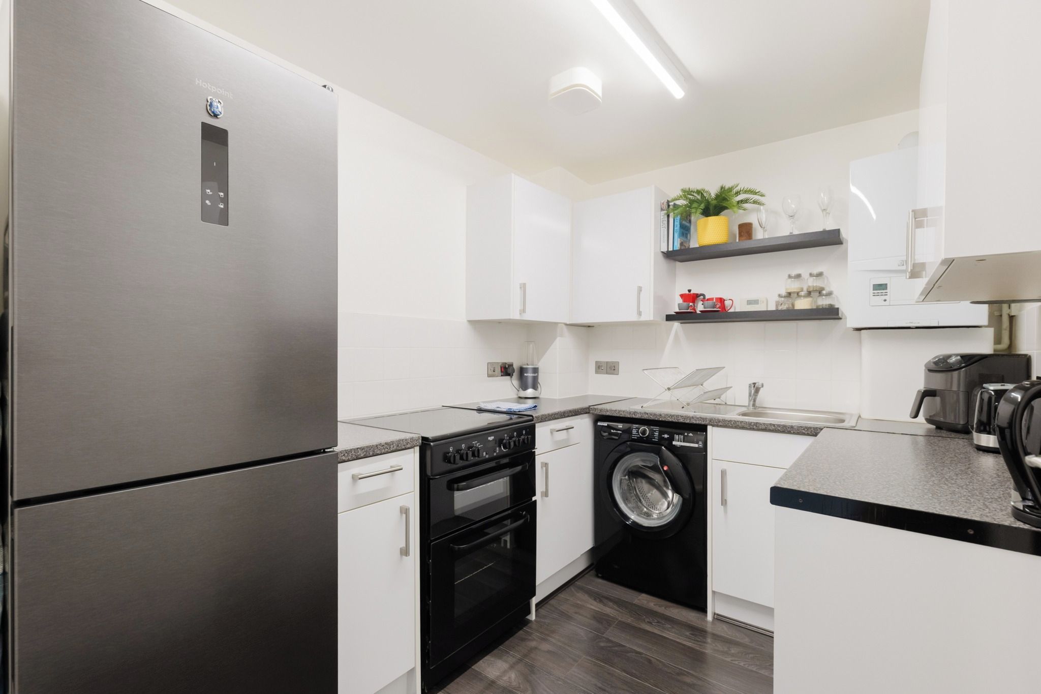 A modern kitchen with a stainless steel refrigerator, a built-in oven, a washing machine, and a coffee maker.