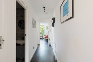A hallway with a view into a bathroom, a door with a handle, and a framed picture on the wall. - Cozy 1BDR City Retreat by Brick Lane (Greater London)