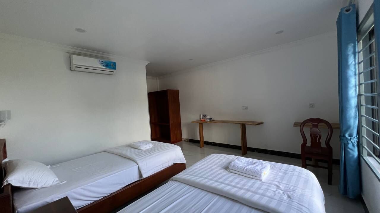 Una habitación con dos camas individuales, un escritorio de madera, una silla y una ventana con cortinas azules.