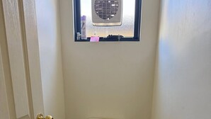 A small, clean bathroom with a toilet, a window with a fan, and a door. - Room-broome Rest House (Broome)