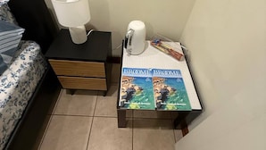 A small room with a bed, a nightstand with a lamp, a kettle, and two books titled 'Drift through Broome'. - Room-broome Rest House (Broome)