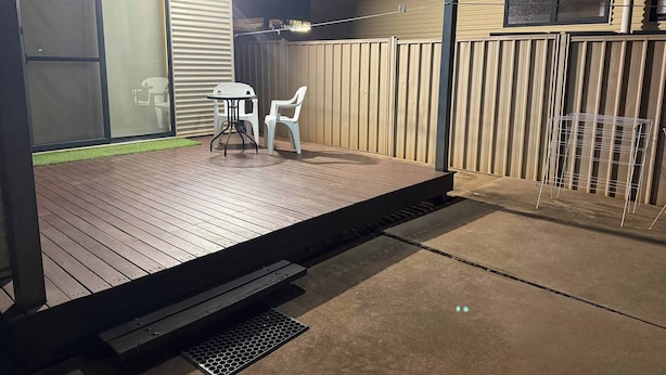A covered patio with a wooden deck, a small table, two chairs, and a metal rack. - Room-broome Rest House (Broome)
