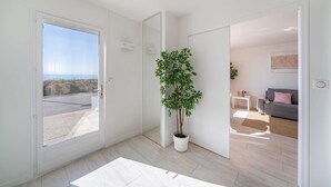 A modern interior with a potted plant, a grey sofa, and a view through a door. - Azur retreat High-End Seafront Apartment (Villeneuve-Loubet)