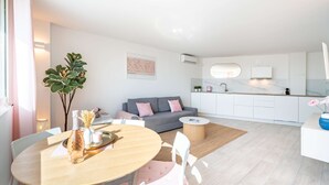 A modern living room with a dining area, a grey sofa, and a kitchen in the background. - Azur retreat High-End Seafront Apartment (Villeneuve-Loubet)