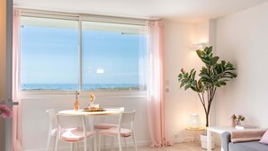 A room with a dining table, chairs, a potted plant, a sofa, and a window with a view. - Azur retreat High-End Seafront Apartment (Villeneuve-Loubet)