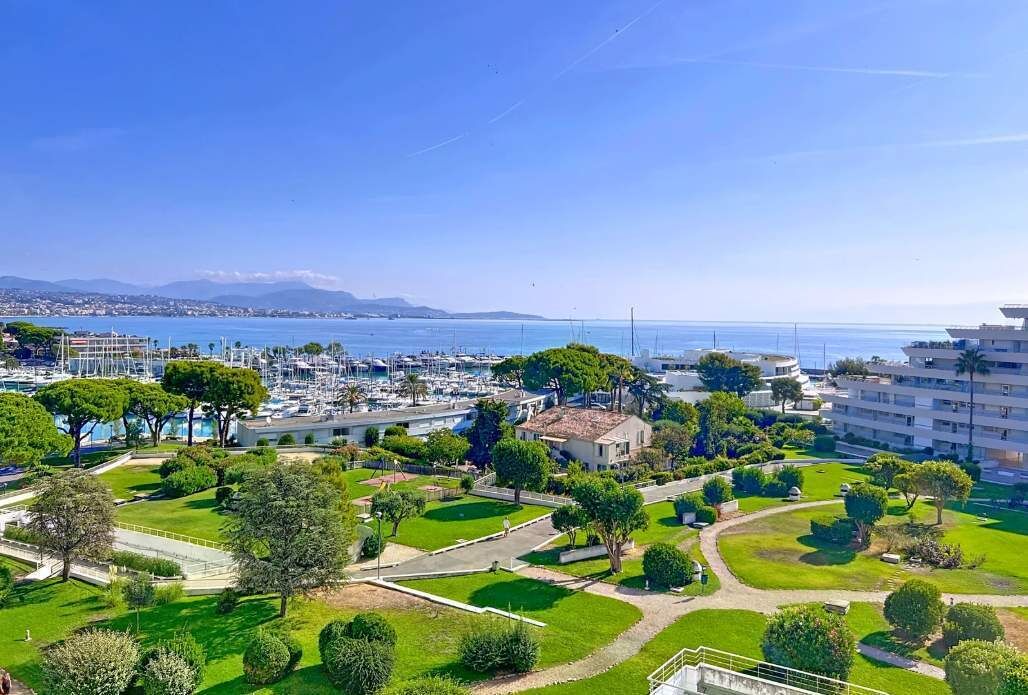 Una marina costanera amb vaixells, cel serena i un parc amb senders i arbres.