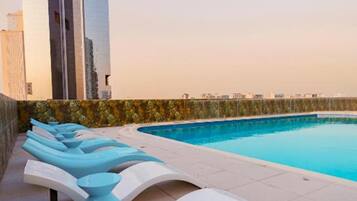 A rooftop pool area with lounge chairs and a view of modern buildings.