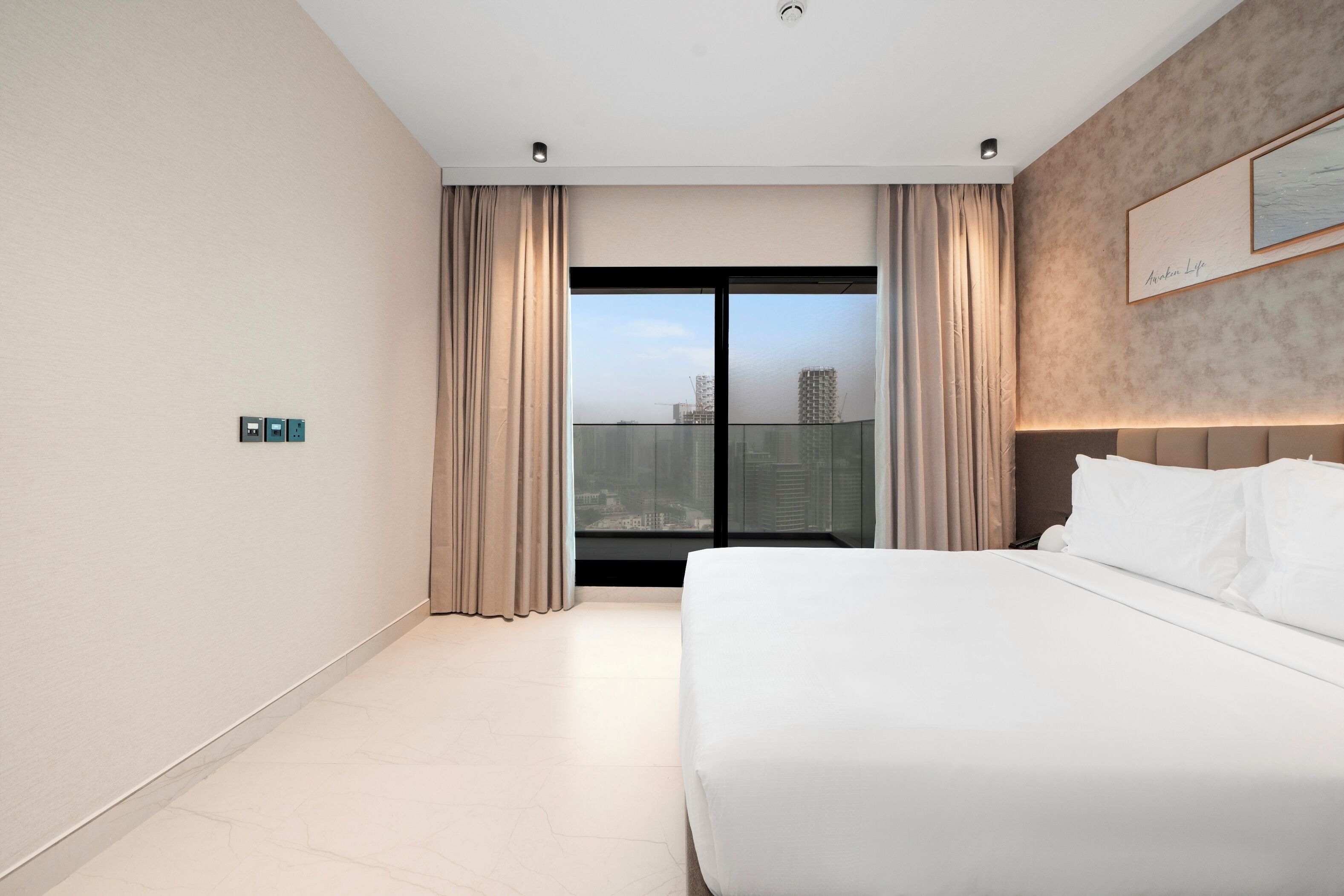A modern hotel room with a large bed, a view of the cityscape through floor-to-ceiling windows, and a minimalist design.