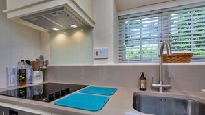 A modern kitchen with a built-in stove, a sink, and a window with blinds.
