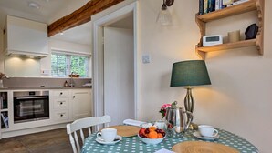 A cozy dining area with a polka dot tablecloth, a lamp, a coffee pot, and a fruit bowl.