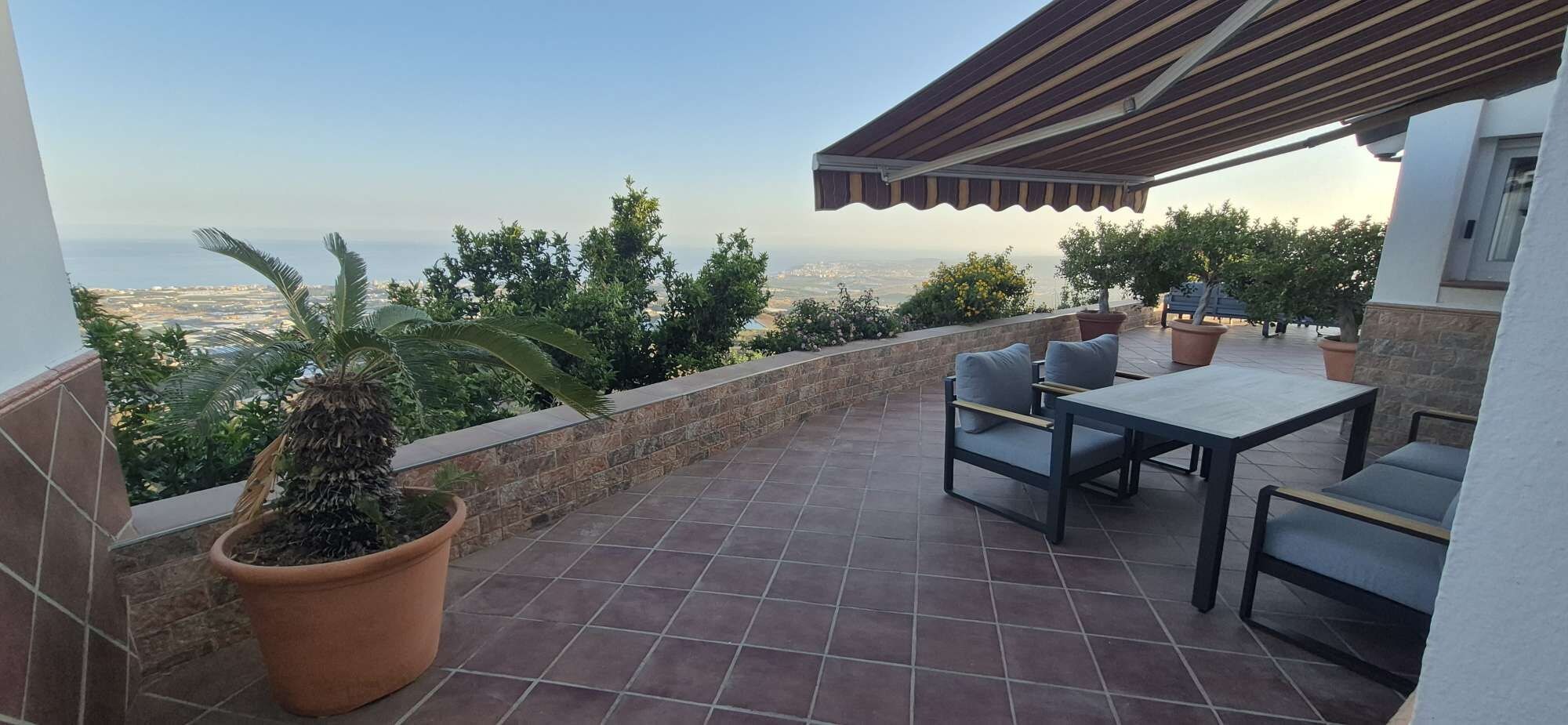 Eine Terrasse mit Tisch und Stühlen, einem Blumentopf und Blick aufs Meer.