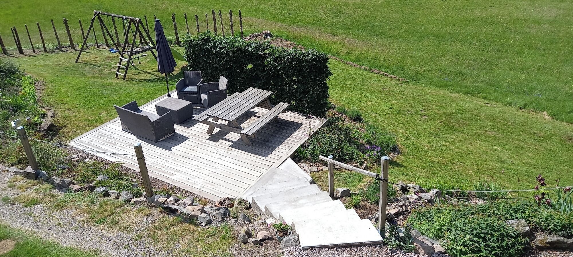 A wooden deck with outdoor furniture, a swing set, and a pathway leading to a grassy area.