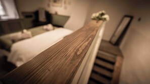 Un dormitorio con cabecera de madera, cama con ropa blanca, mesita de noche y un jarrón con flores.