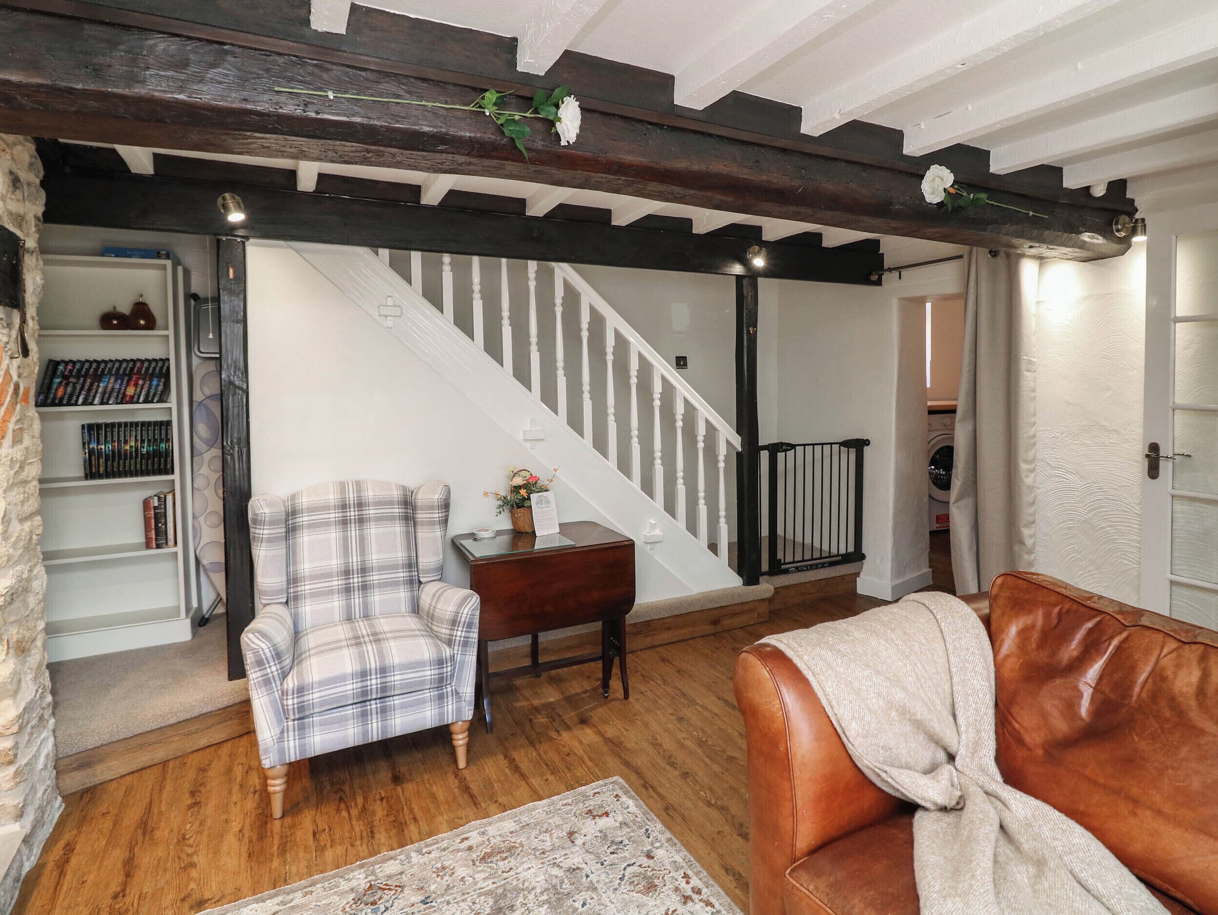 Una sala de estar con una escalera, un sillón escocés, un sofá de cuero y una estantería.