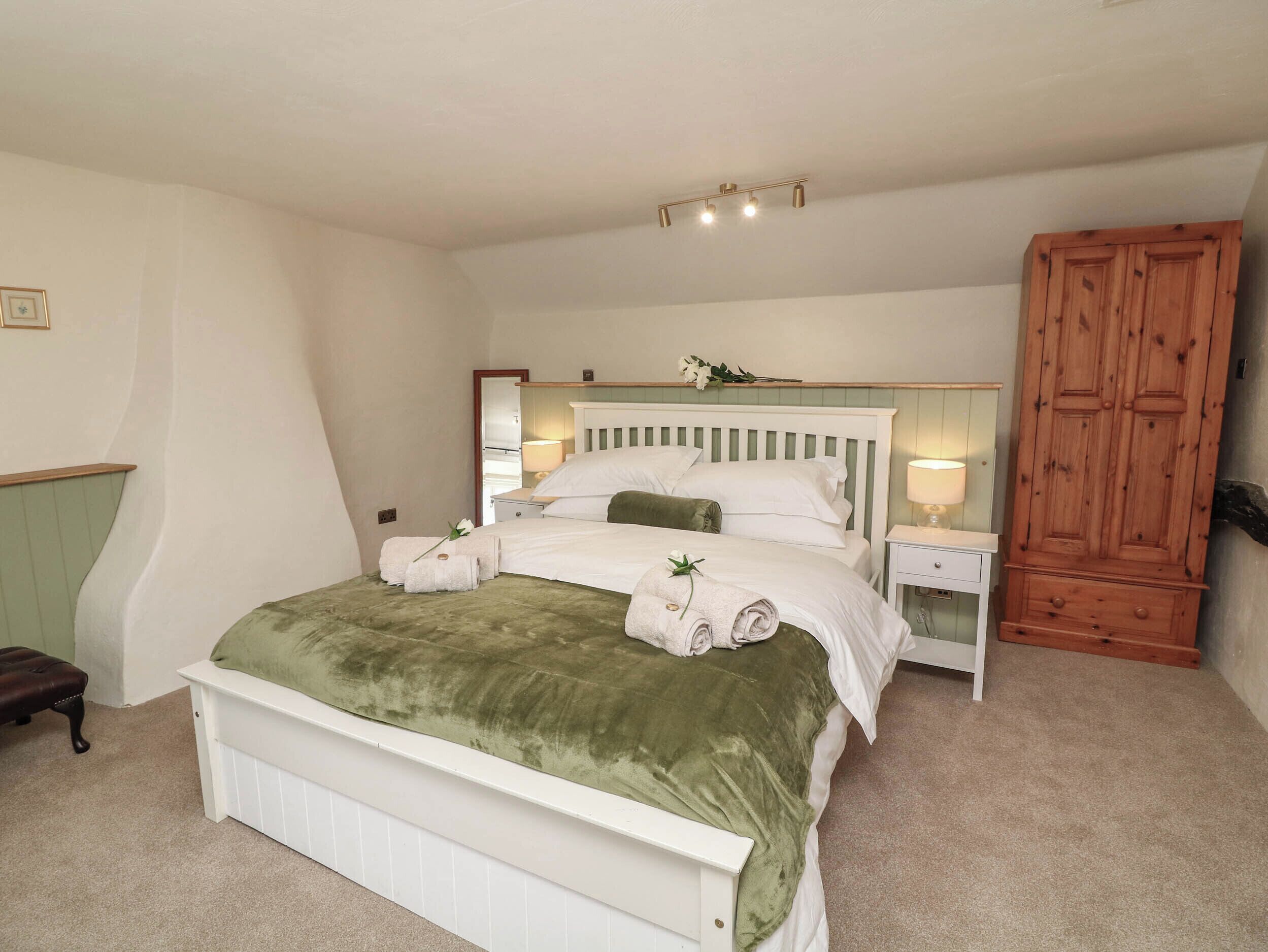 Un dormitorio con cama, mesitas de noche, un armario de madera y un espejo.