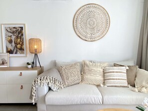 A modern living room with a light-colored sofa, decorative pillows, a woven floor lamp, and a large circular wall hanging. - Balcon del Mar Seaview 211 by Casasol (Nerja)
