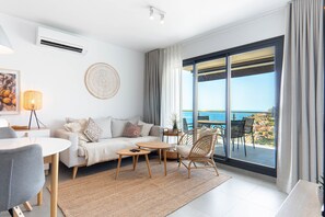 A modern living room with a sofa, coffee table, and chairs, a large window with a view of the sea, and a ceiling fan. - Balcon del Mar Seaview 211 by Casasol (Nerja)