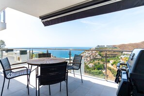 Un balcón con una mesa redonda y sillas, con vistas a un pueblo costero y al mar.