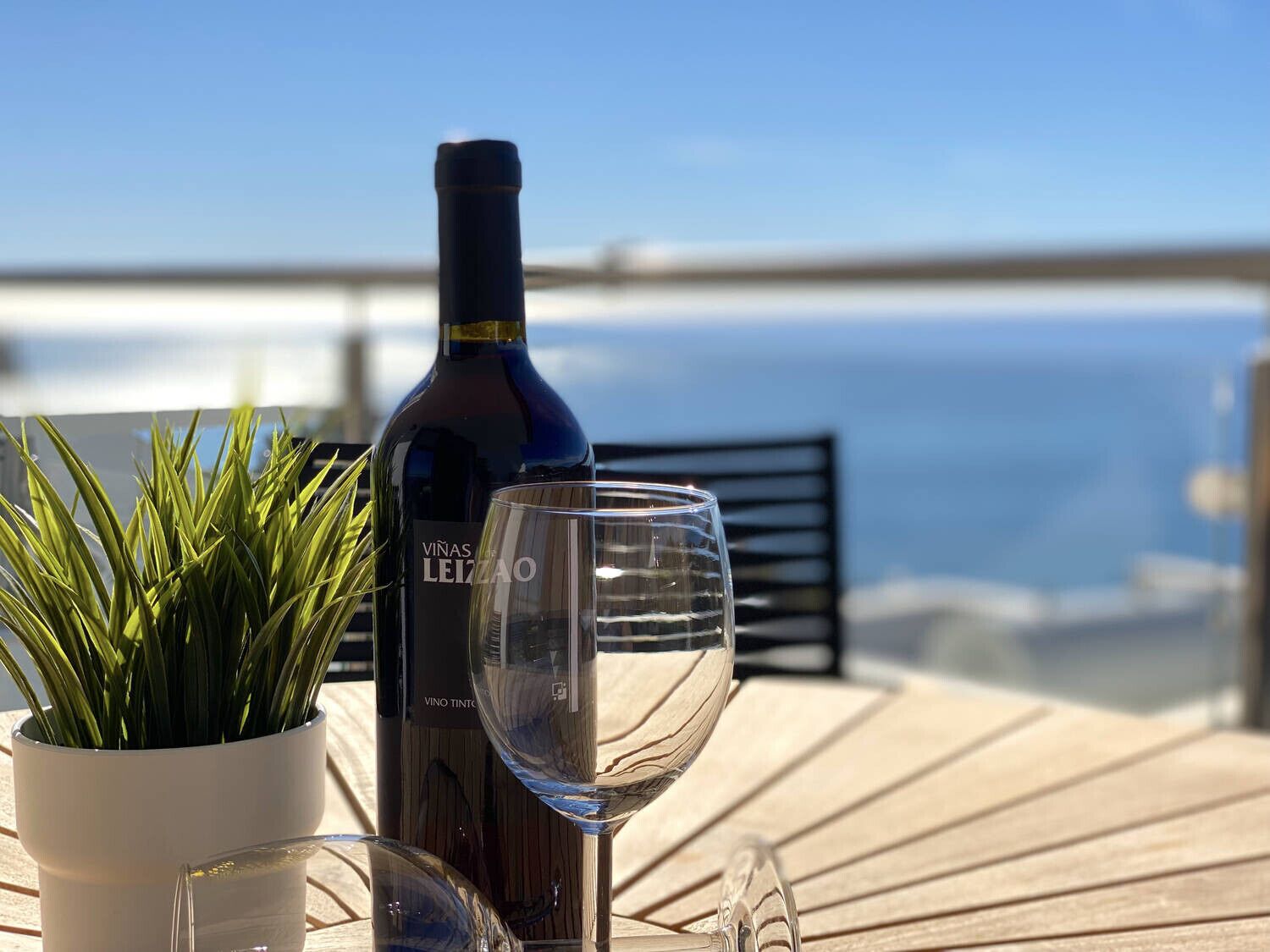 A bottle of Vinas Leizao wine and a glass on a wooden table with a view of the sea.