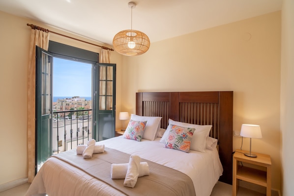 Ein Hotelzimmer mit Bett, Nachttisch, Lampe, Blick auf die Stadt und einem Balkon.