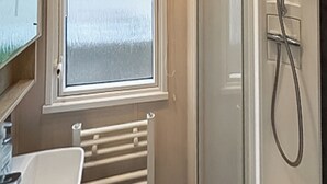 A bathroom with a glass shower enclosure, a white sink, and a window above the sink. - Swift Bordeaux Escape - UKC9640 (Towyn)