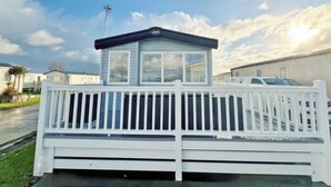 Une maison mobile dotée d’une véranda blanche et d’une petite annexe adjacente avec une fenêtre.