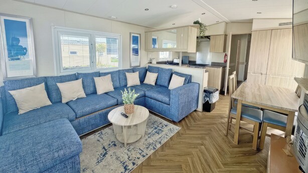 Un salon moderne avec un canapé d’angle bleu, une table basse ronde et un parquet en bois à motifs chevrons.