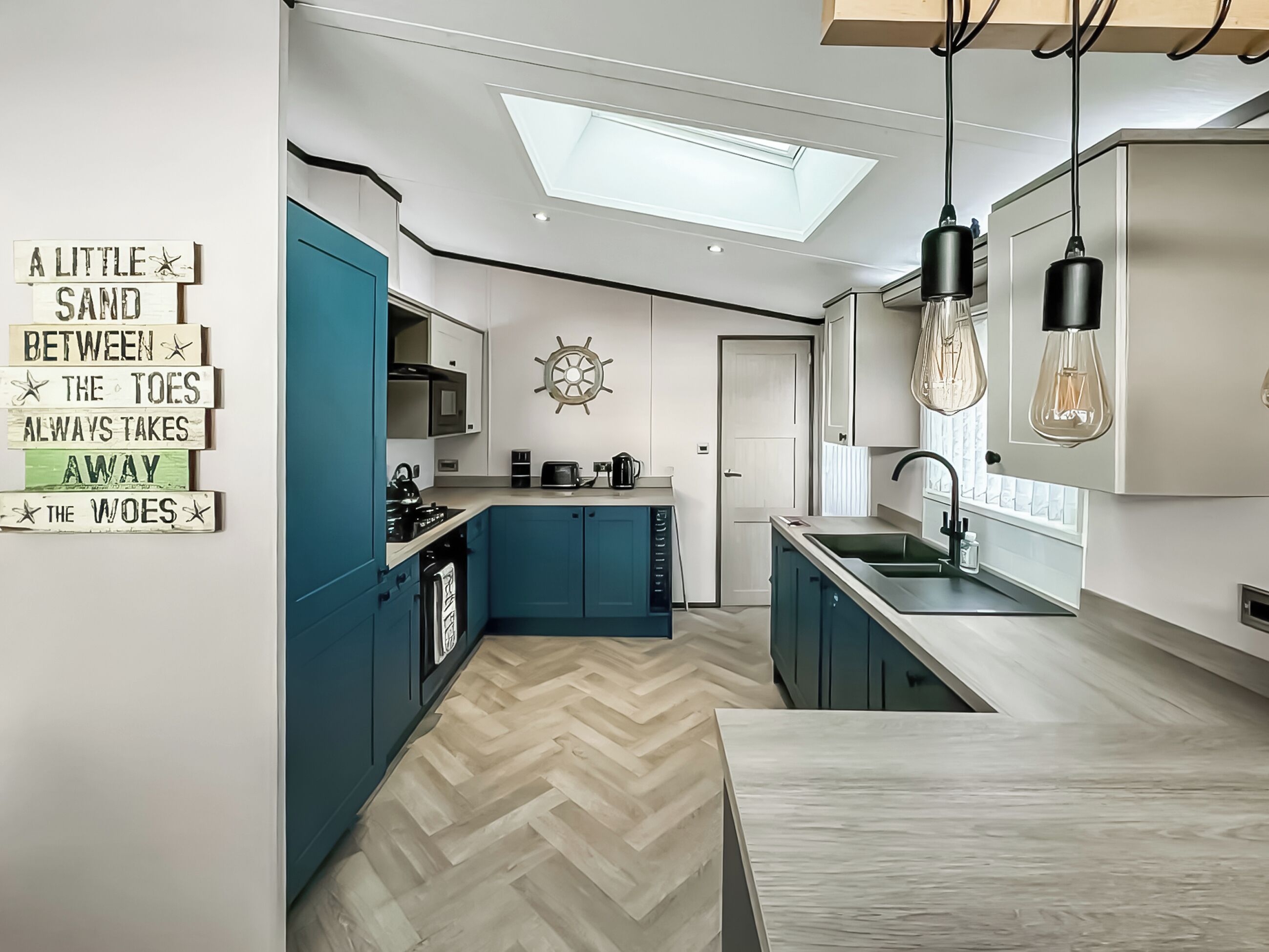 A modern kitchen with teal cabinets, a herringbone floor, a skylight, and a ship's wheel decoration.