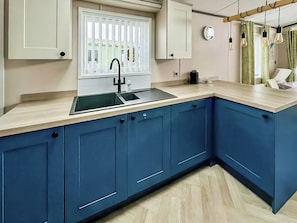 A kitchen with a sink, window, cabinets, and a clock on the wall. - Monaco Duo - UKC9617 (Towyn)
