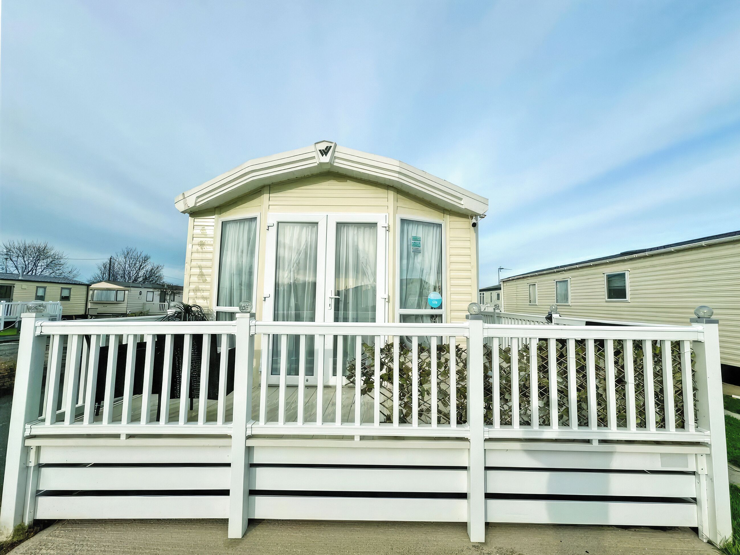 A mobile home with a white exterior, a balcony with a white railing, and a window with a curtain.