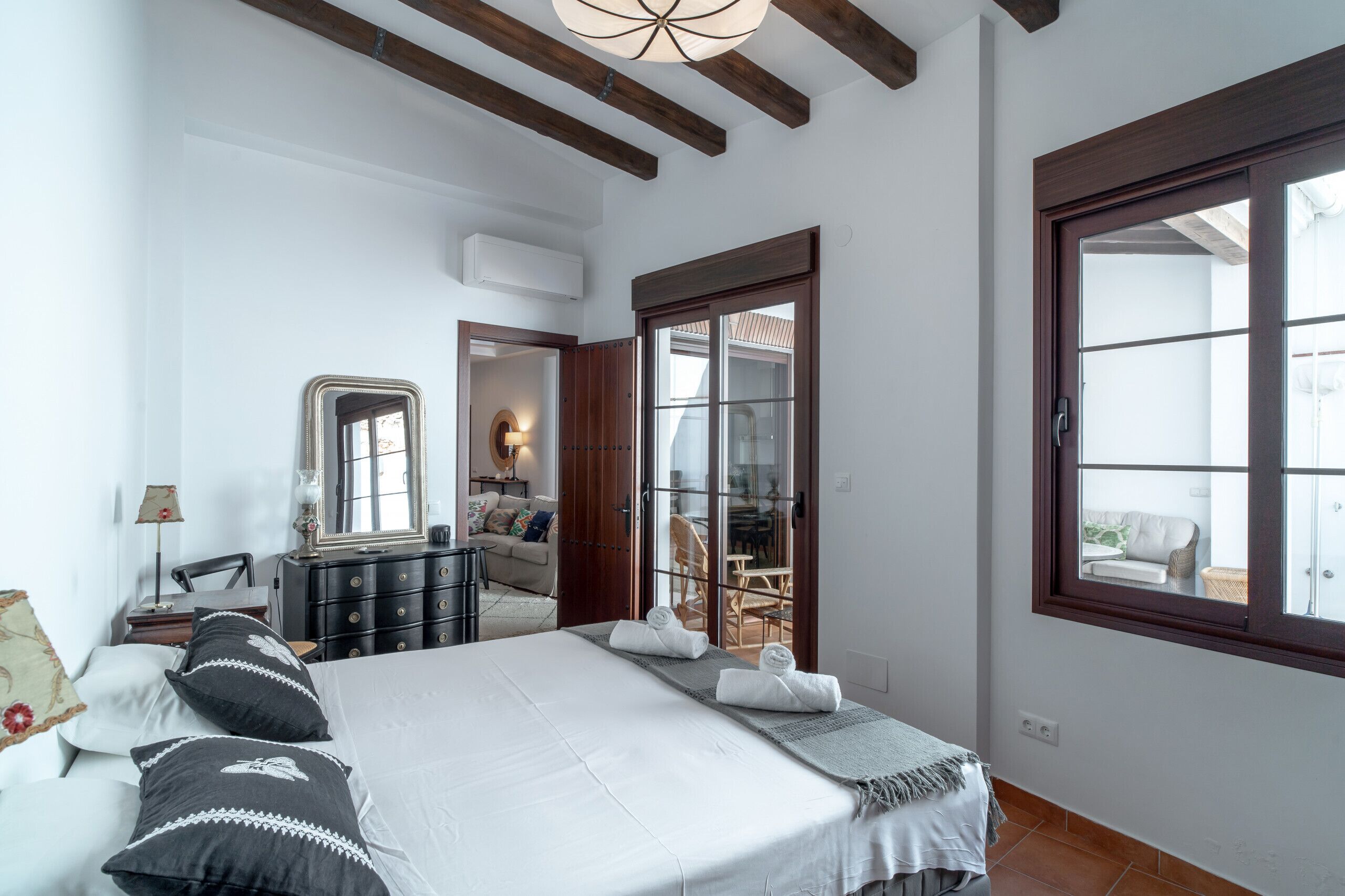 A bedroom with a large bed, a dresser, a mirror, and a sliding glass door leading to a balcony.