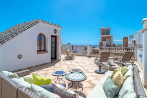 Eine Dachterrasse mit Korbmöbeln, einem kleinen Tisch und Blick aufs Meer.