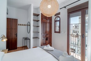 Ein Schlafzimmer mit Bett, einer Hängelampe, einem Holzschrank, einem kleinen Tisch und Blick auf einen Balkon.